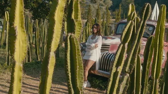Young Asian Woman Stands By an Old Pickup Truck at Sunset and Looks at the Camera alt