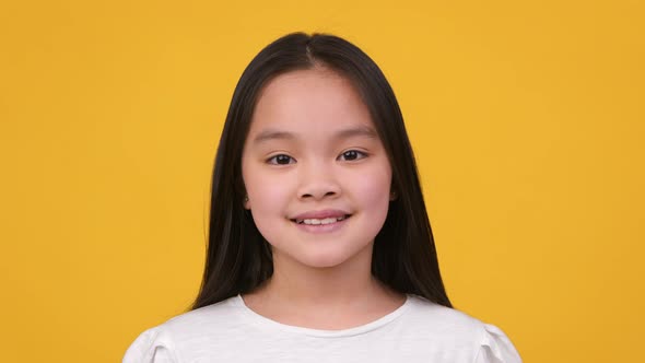 Close Up Studio Portrait of Adorable Pretty Preteen Asian Girl Smiling to Camera Posing Over Orange alt