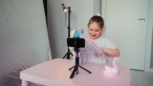 Young little girl blogger writes a video about knitted toys on her blog in a home studio alt