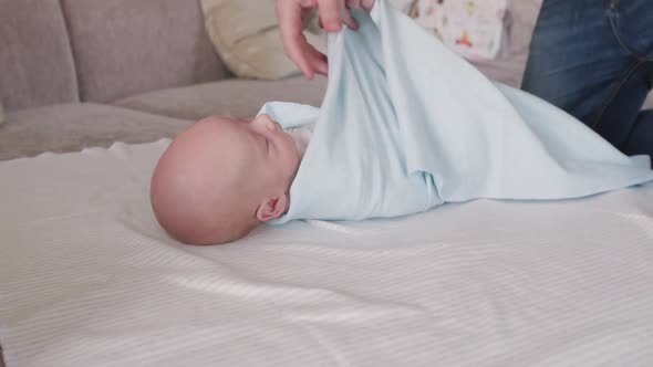 Father Swaddles a Newborn Son in a Blue Diaper alt