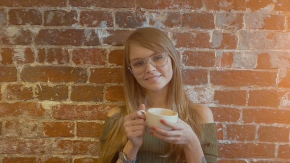 Beautiful Young Smiling Woman with Cup of Hot Coffee Standing Near Brick Wall