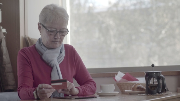 Mature Woman Makes an Online Purchase Using a Tablet in the Cafe.