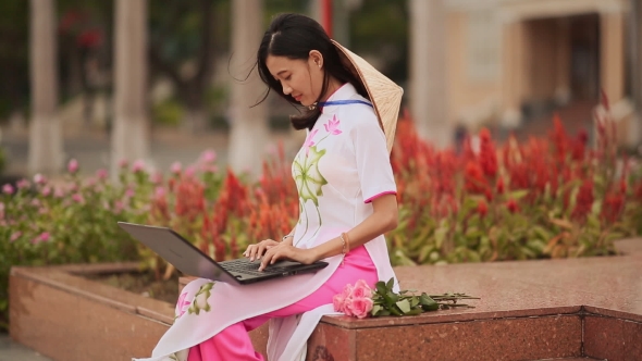 The Beautiful Asian Girl Speaks on a Laptop on the Street and a Beautiful National Dress Ao Dai with alt