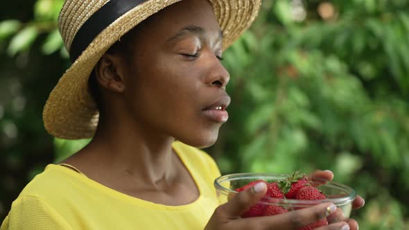 Proud Happy African American Woman Smelling Organic Red Strawberry in Glass Bowl Smiling Looking at alt