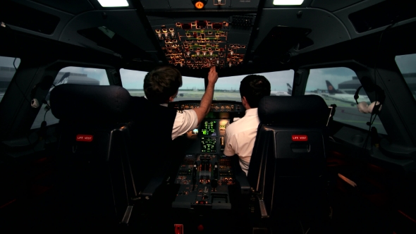 Two Caucasian Male Pilots in the Cockpit or Flight Deck of a Passenger Airplane Switch Controls alt