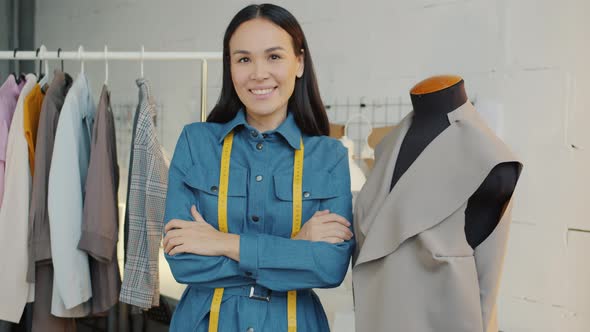 Asian Young Woman Tailor Standing in Showroom Against New Clothes Background alt