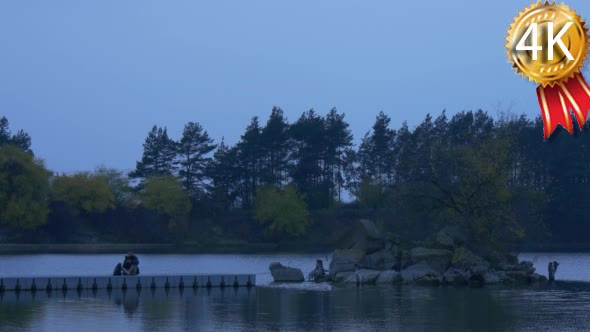 Man Gets up Stands on a Pier Looks at River Stony alt
