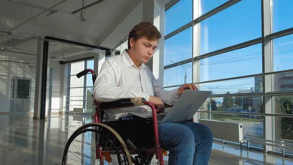 Disabled Businessman on a Wheelchair at a Window with a Laptop