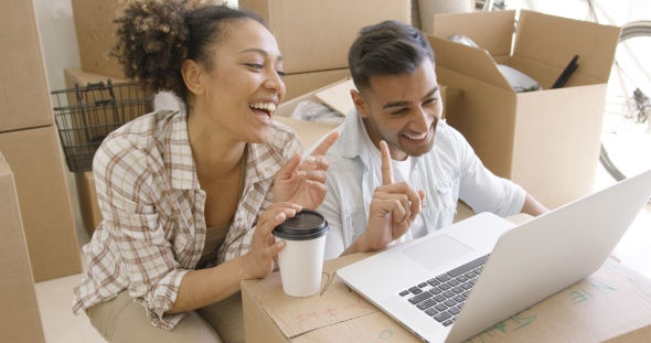 Happy Mixed Race Couple Discuss While Using Laptop alt