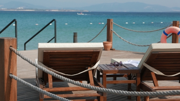 View of the Emty Wooden Sunbeds and Coffee Table with a Sunglasses with Sea and Moving Boat on the