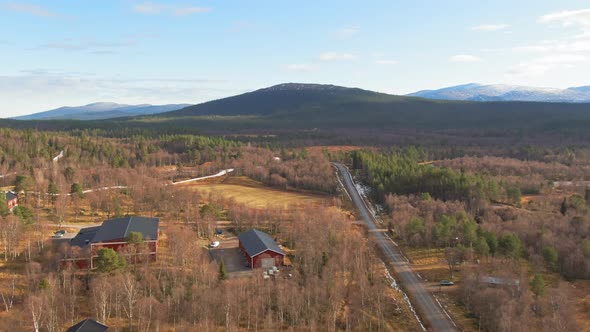 Red Farm Buildings In Swedish Alpine Spruce Conifer Forest Near Snowcapped Mountains. alt