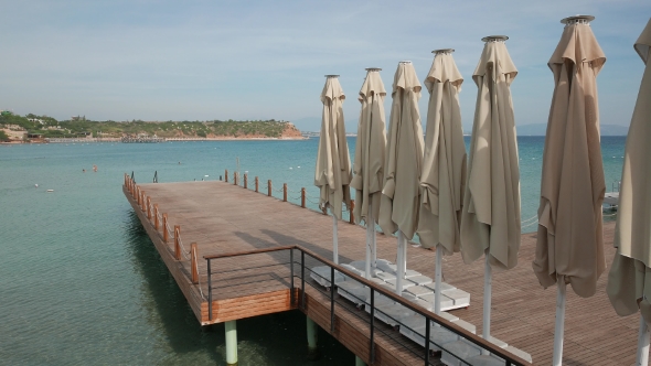 Wooden Bathing Pier with Line of Umbrellas Ready for Swimming Season with Shore and Sea in a Sunny