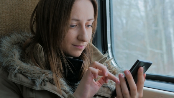 Pensive Woman Traveling on a Train and Using a Smartphone
