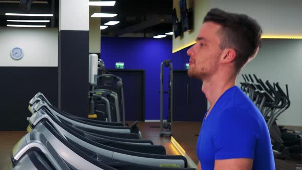 A Young Fit Man Walks on a Treadmill in a Gym - Closeup From Side alt