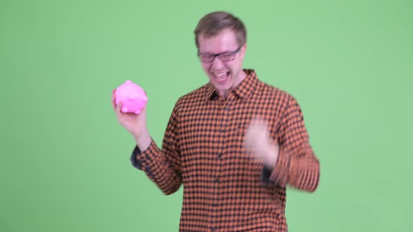 Happy Young Hipster Man Turning Around While Holding Piggy Bank and Dancing alt