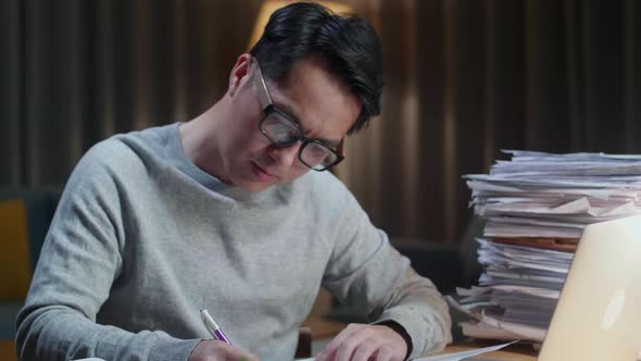 Close Up Of Asian Man Looking At Laptop And Taking Note While Working With Documents At Home alt