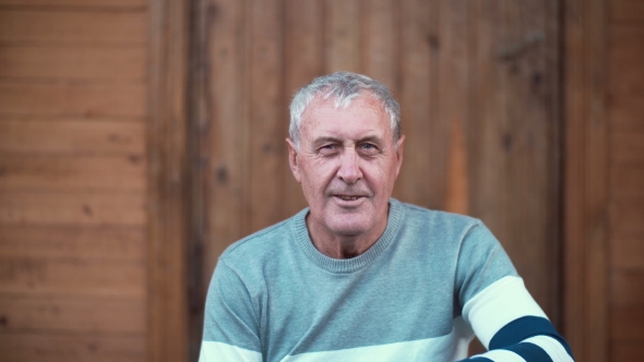 Portrait of Old Man Sitting on the Porch of the House. Pensioner Looking To the Camera, Smiling and alt