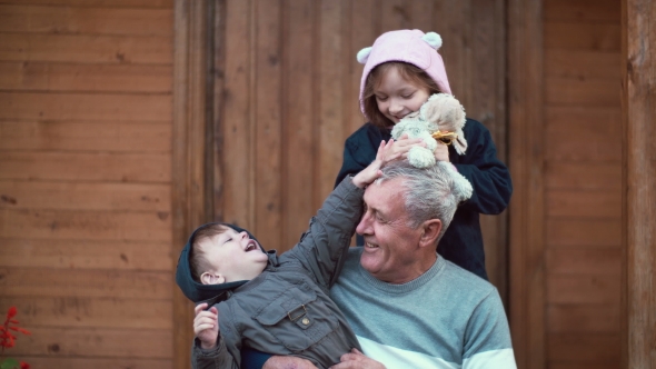 Boy Sitting on Grandfather Knees, Girl Standing Behind and Hug. Brother and Sister Playing with Toy alt