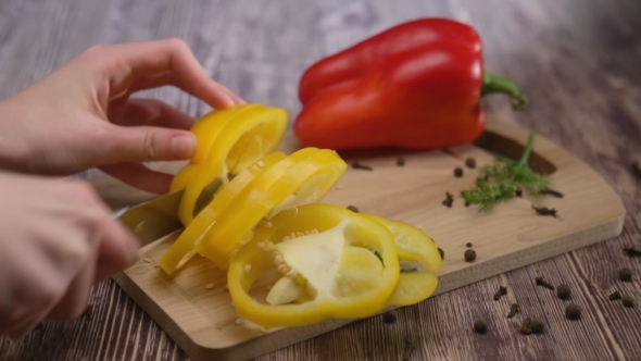 Woman Hands Cuts Pepper on a Wooden Table