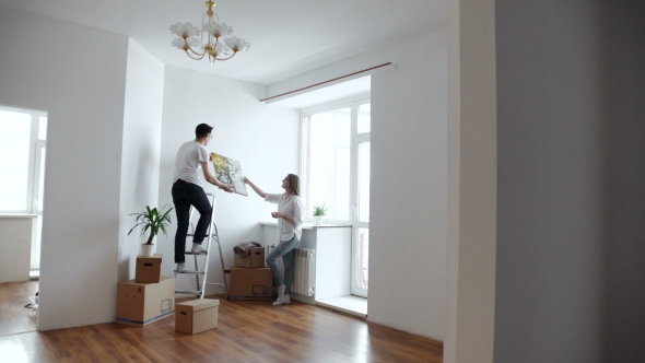 Happy Couple Hanging Picture on the Wall at Home alt