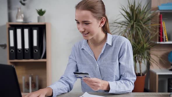 Woman Sitting at the Table and Making Online purchases using laptop and her credit card alt