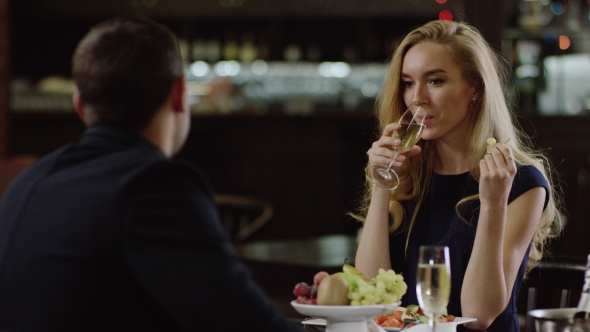 Romantic Girl Drinking Champagne in Restaurant and Eating Grapes