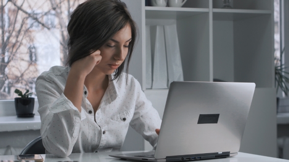 Tired Woman in a Works at a Laptop in the Office alt