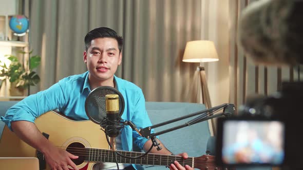 Asian Man Is A Vlogger With Guitar Looking To Camera While Live Streaming alt
