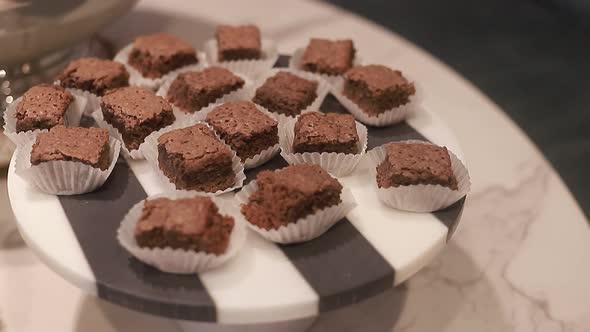 Young woman take of round plate with baked brownies, delicious chocolates biscuits, close up shot. alt