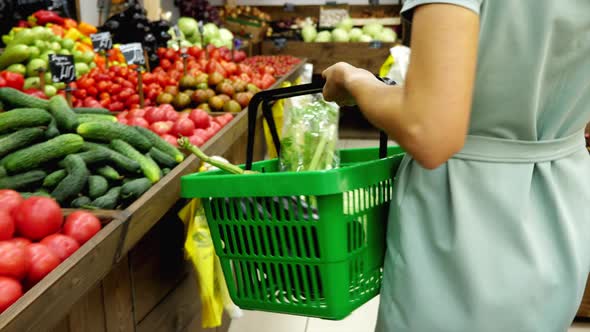 Woman with shopping basket walking along rows in grocery and taking vegetables