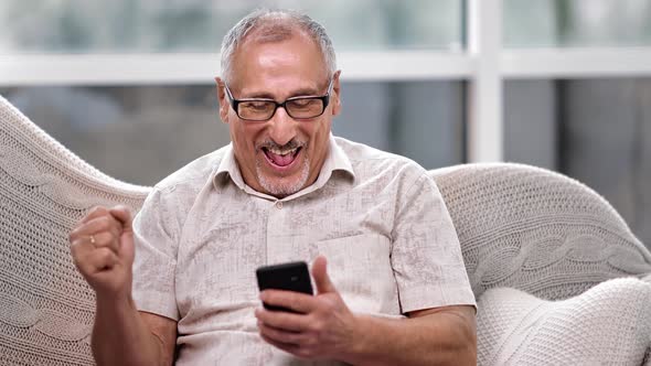 Happy 70s Grandfather Winner Mobile App Sport Bet Holding Smartphone alt