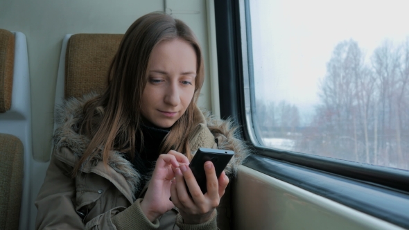 Pensive Woman Traveling on a Train and Using a Smartphone alt