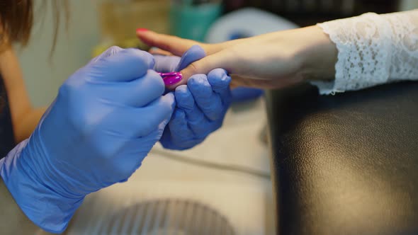 Unrecognizable Person in Gloves Paints Nails of Young Woman in Salon alt