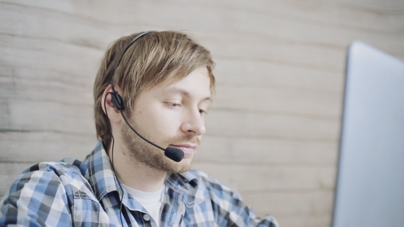 Young Tired Male Operator of Call Center with Headset Using Laptop