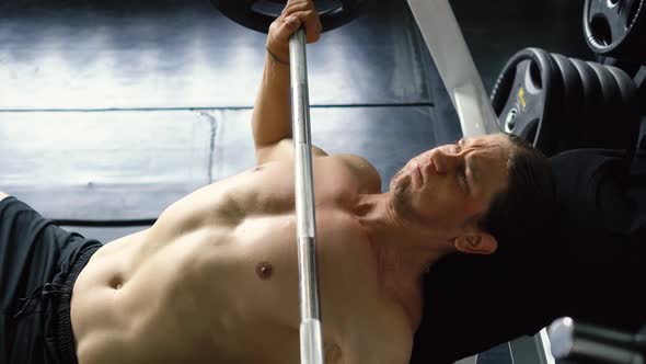 Shirtless Muscular Man Doing Barbell Bench Press Exercise at the Gym alt