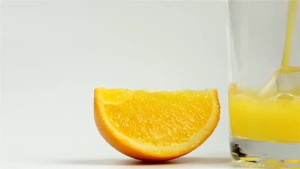 Fresh Orange Juice Is Poured Into A Glass And A Slice Of Orange Next To A White Background Close