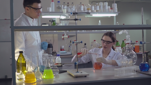 Chemist Engineer Holding Flasks Adding Liquid To Test-tubes With. alt