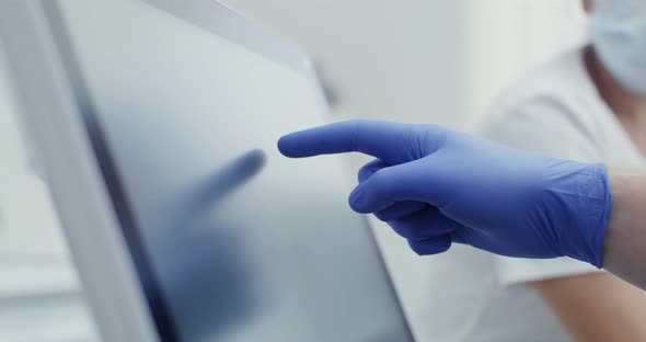 A Doctor in Hygienic Gloves Uses a Tablet Moving His Finger Across the Screen alt