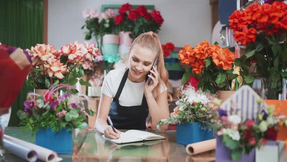 Florist Female Discusses the Order By Talking on the Mobile Phone and Using a Notepad in a Flower alt
