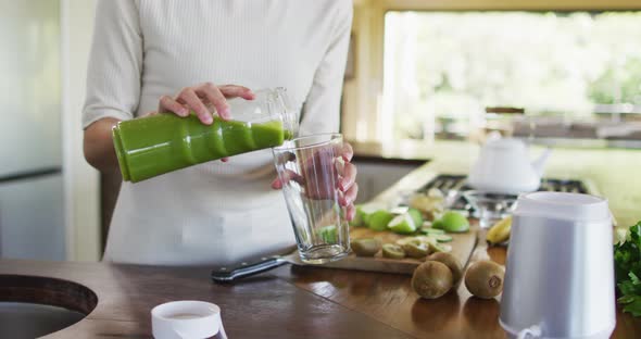 Midsection of biracial woman pouring smoothie to glass in kitchen alt