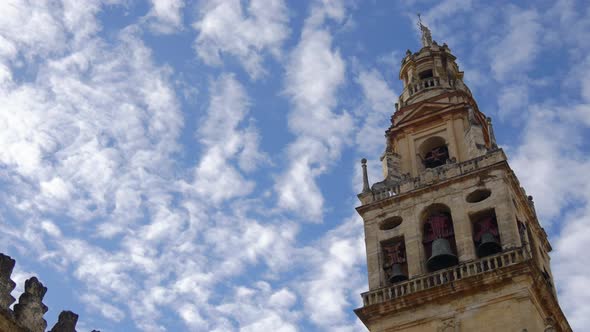 Low angle shot of the Cordoba Mosque Tower with a sky full of white clouds alt