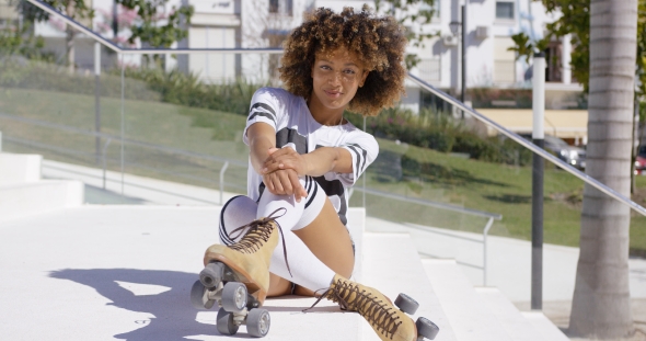 Smiling Female Sitting on Stairs Wearing Rollerskates alt