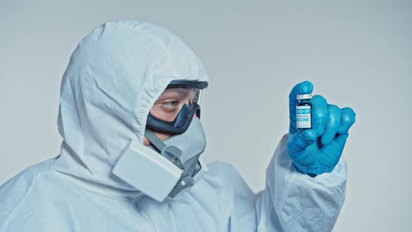 Close-up a Masked Scientist Who Developed a Coronavirus Vaccine Holds an Ampoule of Blue Liquid and alt
