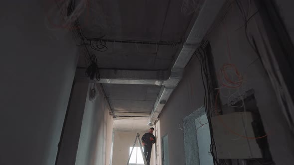 Silhouette of a Construction Worker Laying Ventilation Ducts. Worker Working on a Ladder in a New alt