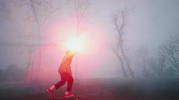 Young Man is Riding a Skateboard in the Evening Holding a Burning Torch in One Hand alt