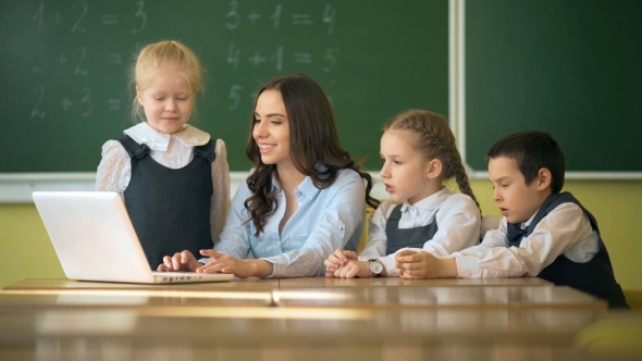 Happy Teacher Using Laptop with Pupils in the Classroom alt