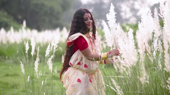 An innocent and playful married Indian bengali woman wearing saree plays with the long white grass i alt