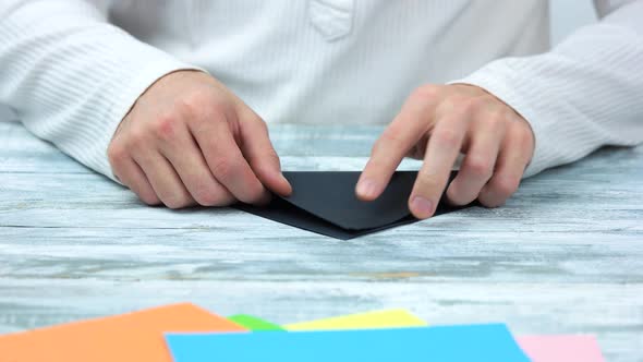 Hands Folding Black Paper Sheet. alt