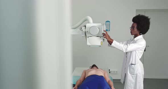 Hospital Man Lying on a Bed Female Technician Adjusts XRay Machine alt