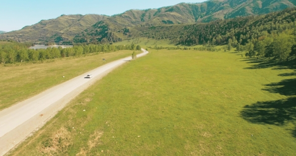 Flight Over Cars on a Winding Road in the Hills and Meadow. Rural Highway Below.